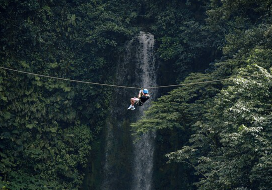 A zipliner crossing in front of a tall jungle waterfall near La Fortuna